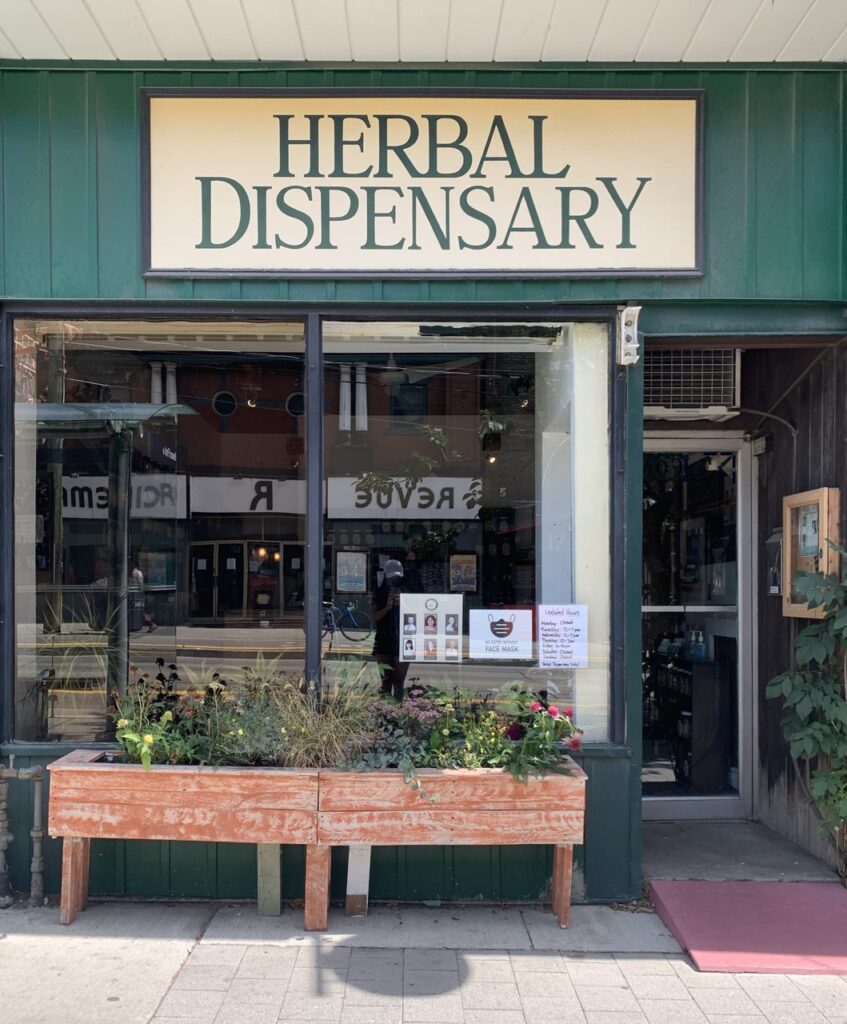herbal dispensary storefront with cream sign green background glass windows, wooden planter and accessibility ramp