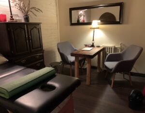 clinic office space with massage table, cupboard, 2 chairs, table and lamp